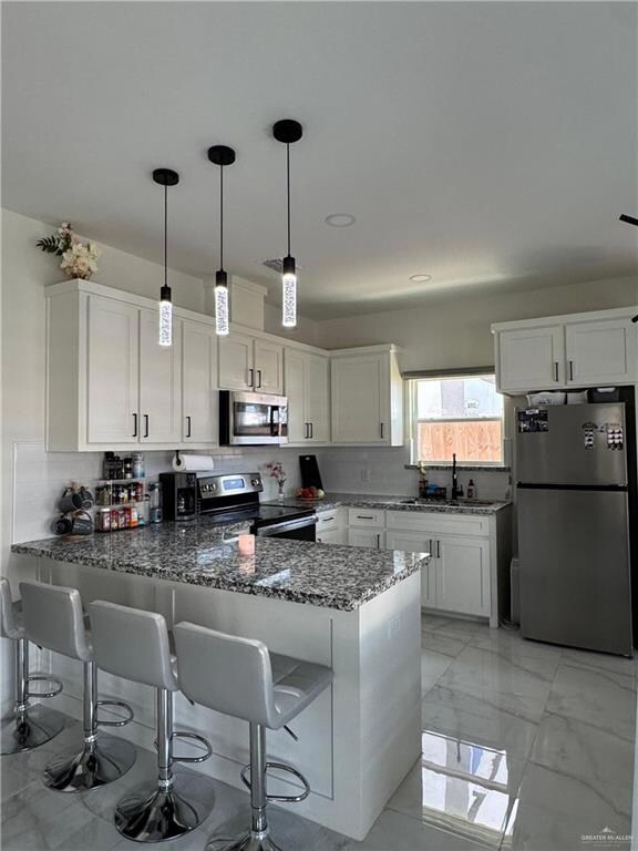 Kitchen with stainless steel appliances, a peninsula, dark stone counters, and white cabinetry