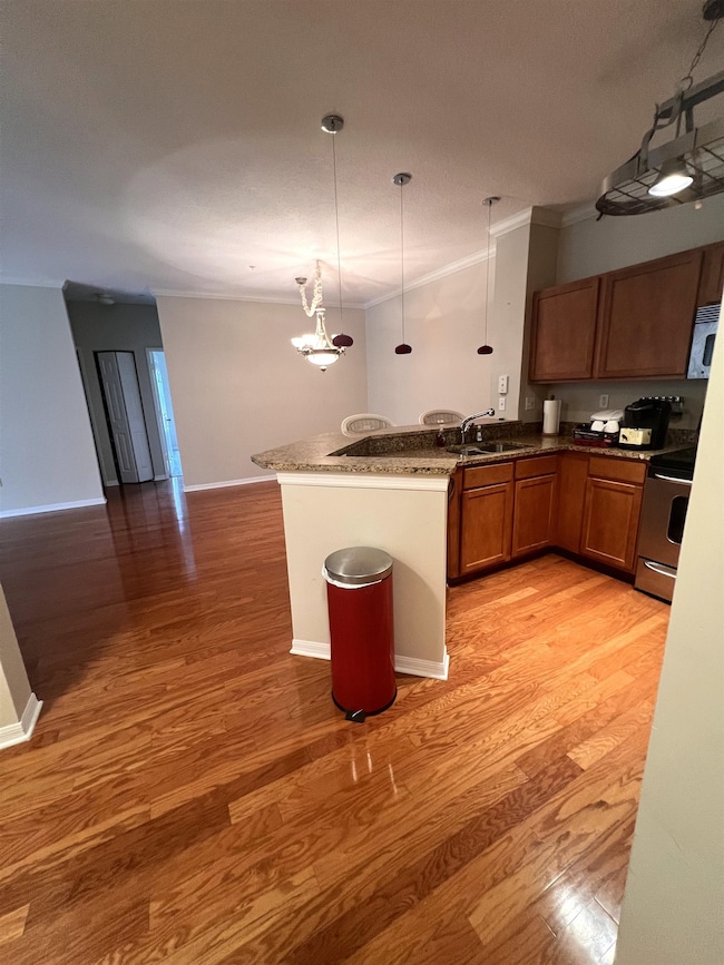 Kitchen featuring pendant lighting, brown cabinets, ornamental molding, a peninsula, and light wood-type flooring