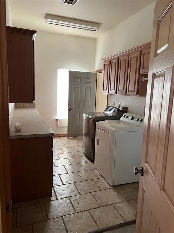 Washroom with washer and clothes dryer, visible vents, cabinet space, and stone tile flooring