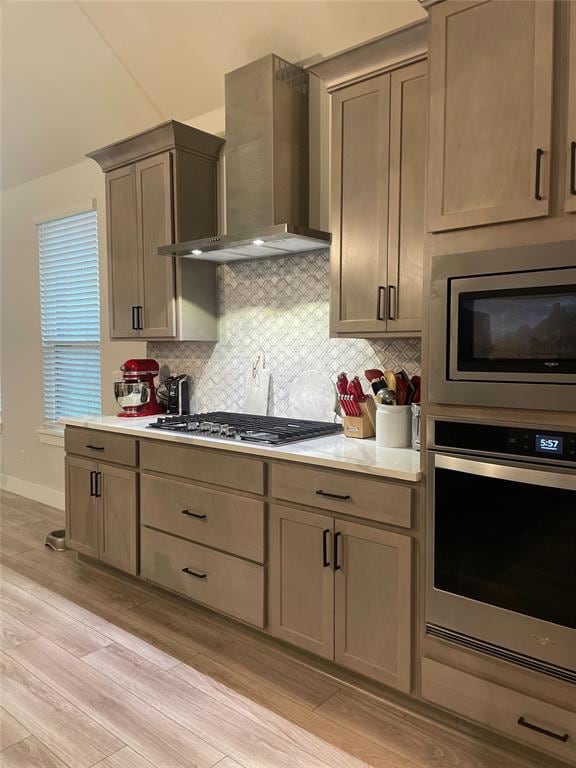 Kitchen featuring light hardwood / wood-style floors, appliances with stainless steel finishes, wall chimney range hood, and tasteful backsplash