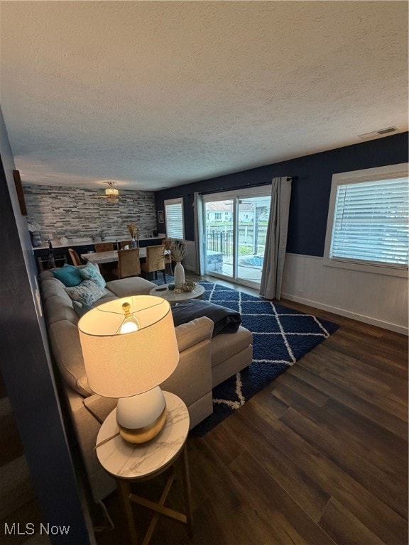 Living area with dark wood-style flooring, a textured ceiling, and wainscoting