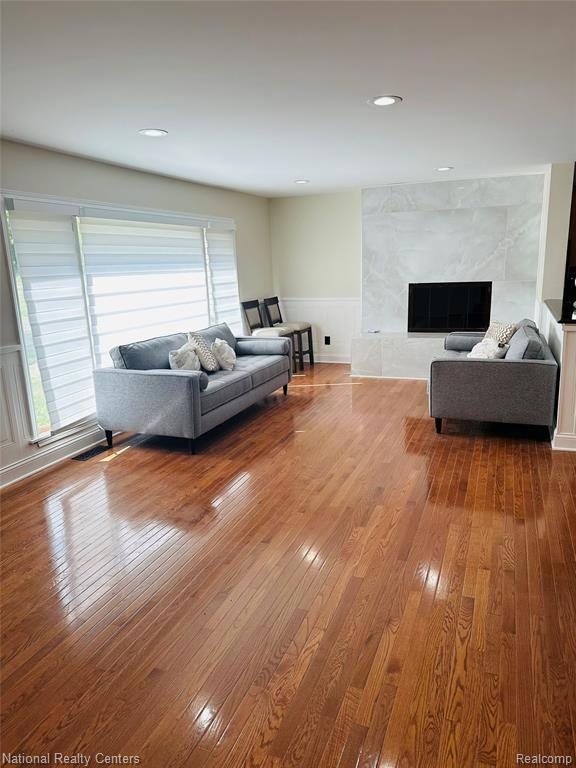 Living room with a wainscoted wall, hardwood / wood-style flooring, a high end fireplace, a decorative wall, and recessed lighting