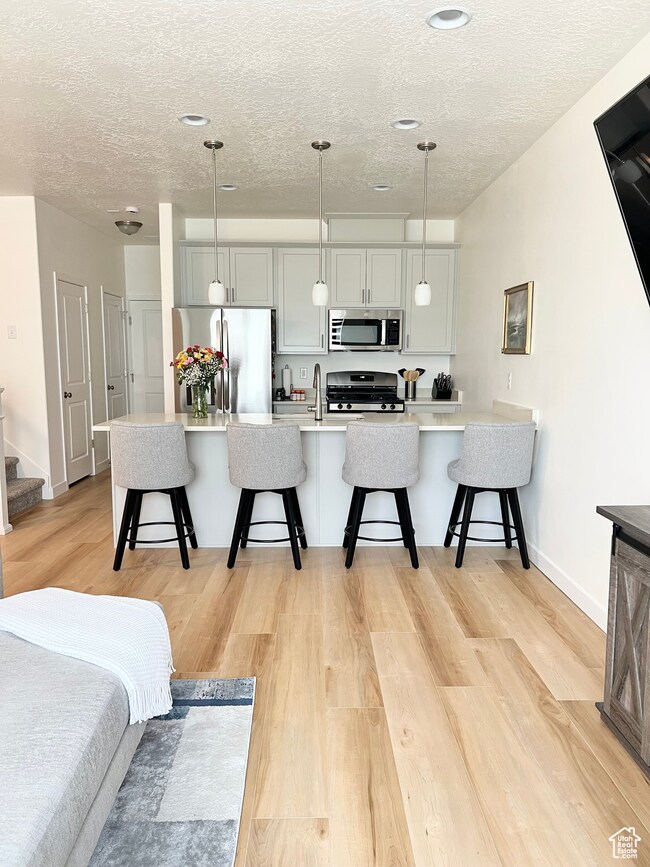 Kitchen with appliances with stainless steel finishes, a textured ceiling, a kitchen breakfast bar, light wood-style flooring, and light countertops