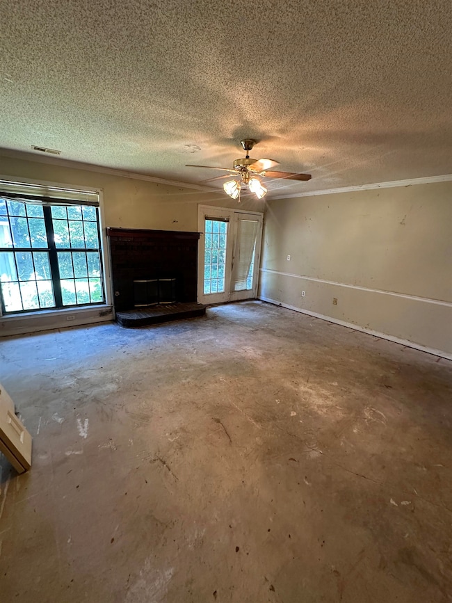 Unfurnished living room with concrete flooring, a textured ceiling, a ceiling fan, and a fireplace with raised hearth