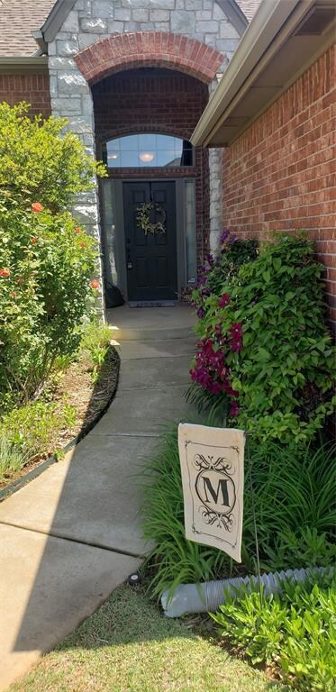 View of exterior entry, mature yard with flowers