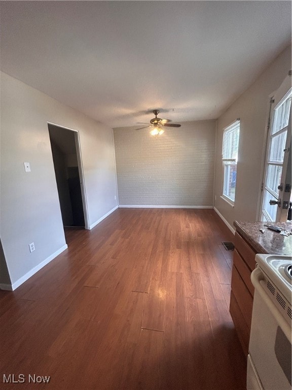 Unfurnished living room with dark wood-type flooring, brick wall, and ceiling fan