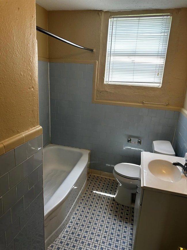 Full bath featuring tile walls, vanity, wainscoti