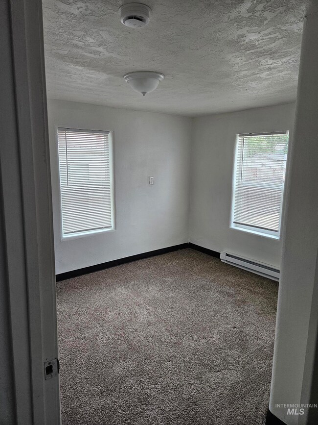 Carpeted spare room featuring a baseboard radiator, plenty of natural light, a smoke detector, and a textured ceiling