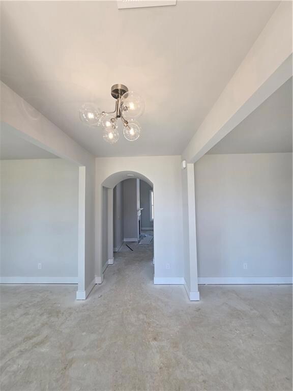 Foyer with arched walkways, unfinished concrete flooring, and a chandelier