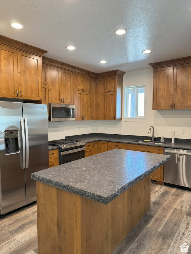 Kitchen with dark countertops, stainless steel appliances, brown cabinetry, a center island, and a textured ceiling
