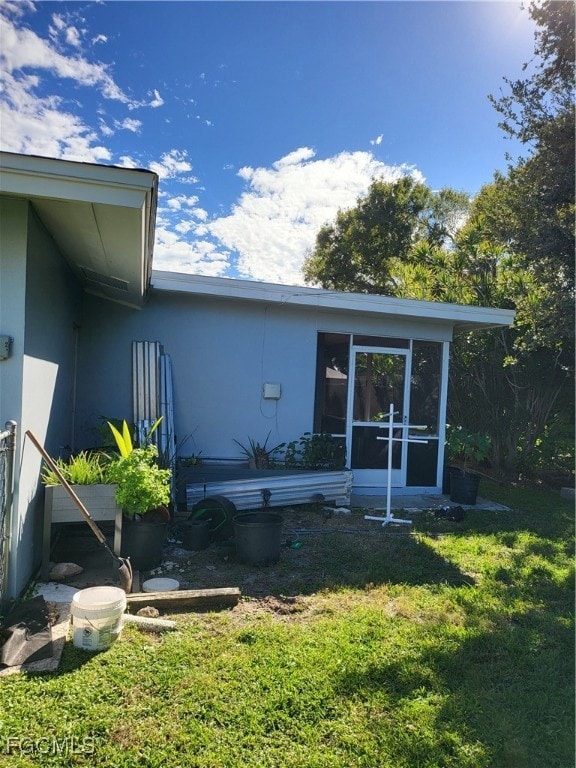 Back of property featuring stucco siding, a lawn, and a sunroom