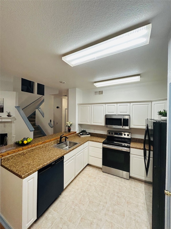 Kitchen featuring a peninsula, black appliances, white cabinets and dark stone counters.