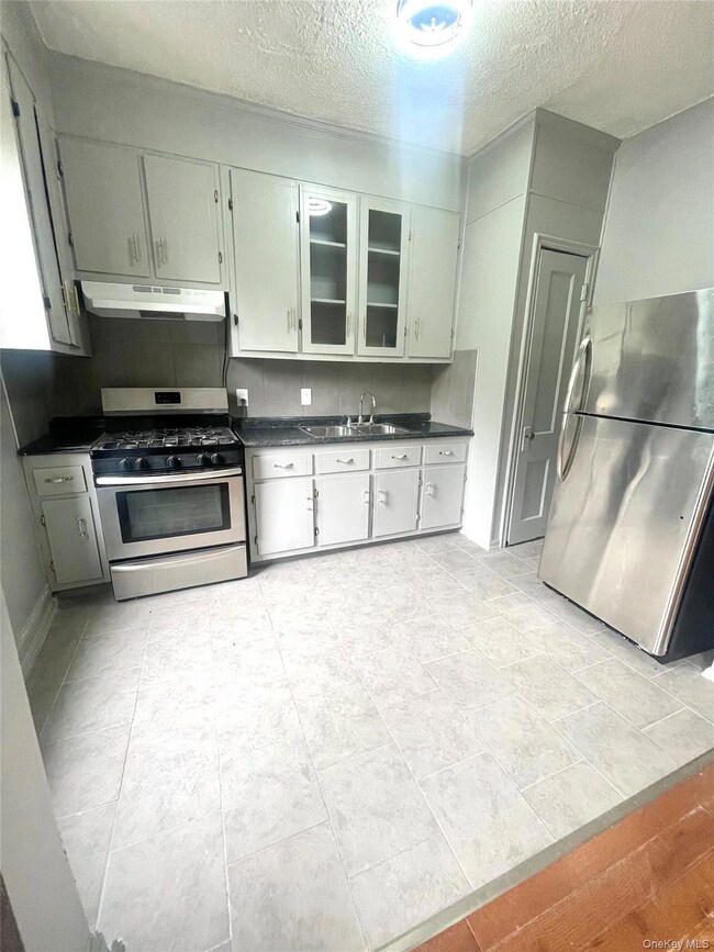 Kitchen featuring dark countertops, stainless steel appliances, a textured ceiling, under cabinet range hood, and light tile patterned flooring