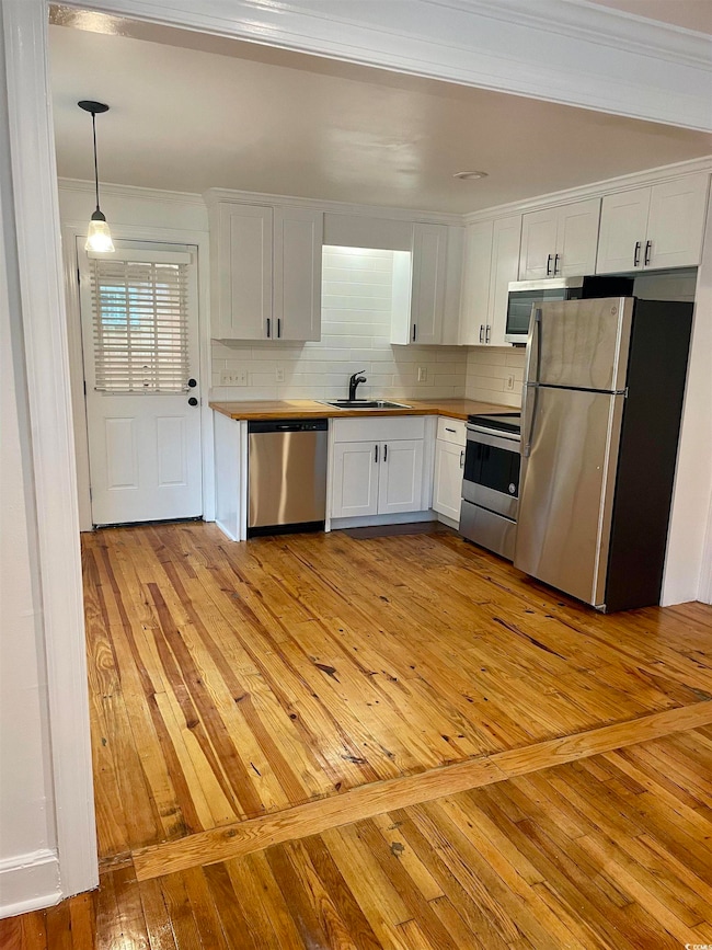 Kitchen featuring light wood-type flooring, white cabinetry, stainless steel appliances, tasteful backsplash, and crown molding