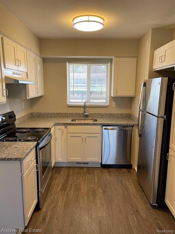 Kitchen featuring stainless steel appliances, white cabinetry, light stone countertops, and dark wood-type flooring
