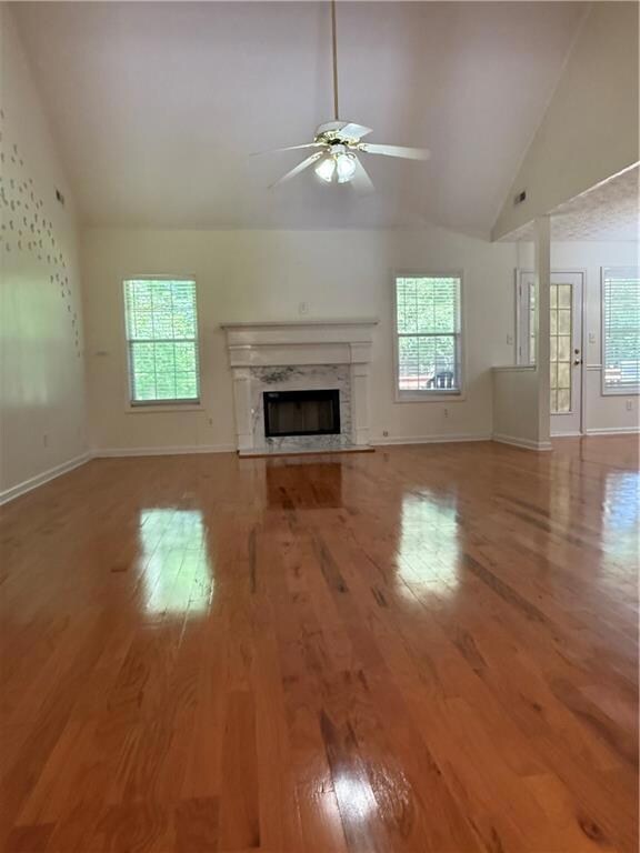 Unfurnished living room with ceiling fan, high vaulted ceiling, light wood-style floors, and healthy amount of natural light