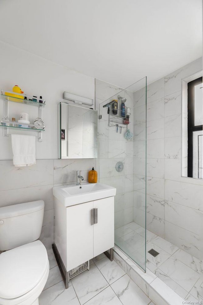 Bathroom with vanity, a shower stall, tile walls, and light marble finish floors