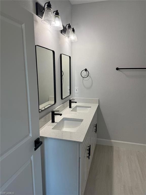 Bathroom featuring wood finished floors, double vanity, and baseboards