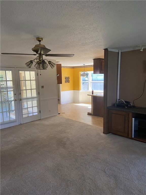 Unfurnished living room with a textured ceiling, light colored carpet, a ceiling fan, and french doors