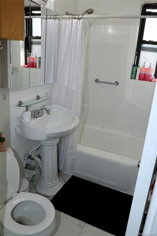 Bathroom featuring shower / bath combo with shower curtain and marble finish floors