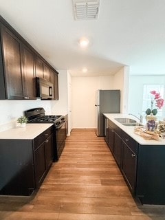 Kitchen with black appliances, light wood-style floors, a center island with sink, and dark brown cabinets
