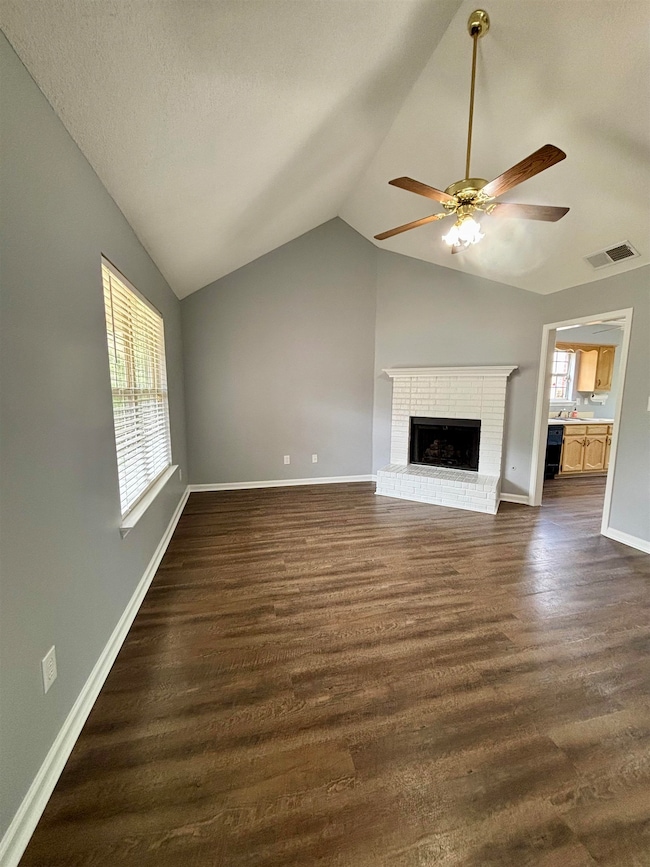 Unfurnished living room featuring lofted ceiling, a ceiling fan, dark wood-style floors, a fireplace, and baseboards