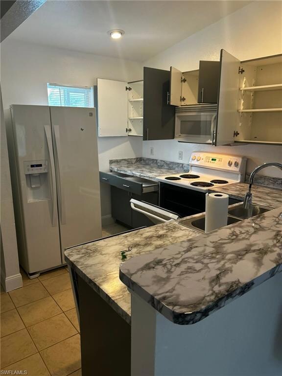 Kitchen featuring white appliances, open shelves, a peninsula, light tile patterned floors, and white cabinetry