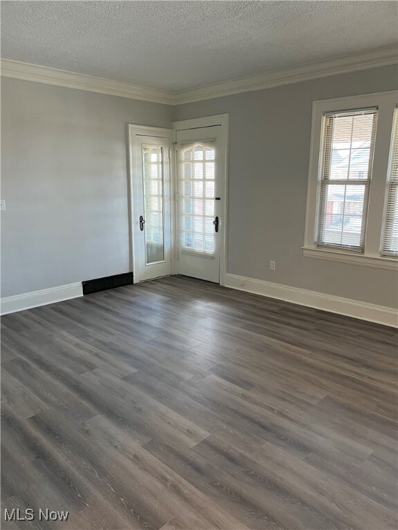 Empty room with a healthy amount of sunlight, a textured ceiling, dark wood-type flooring, and ornamental molding