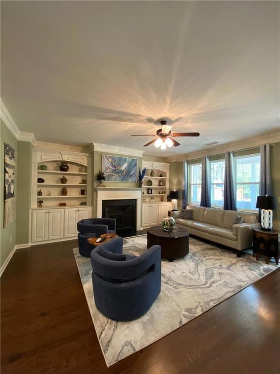 Living area featuring crown molding, built in shelves, ceiling fan, a fireplace, and wood finished floors