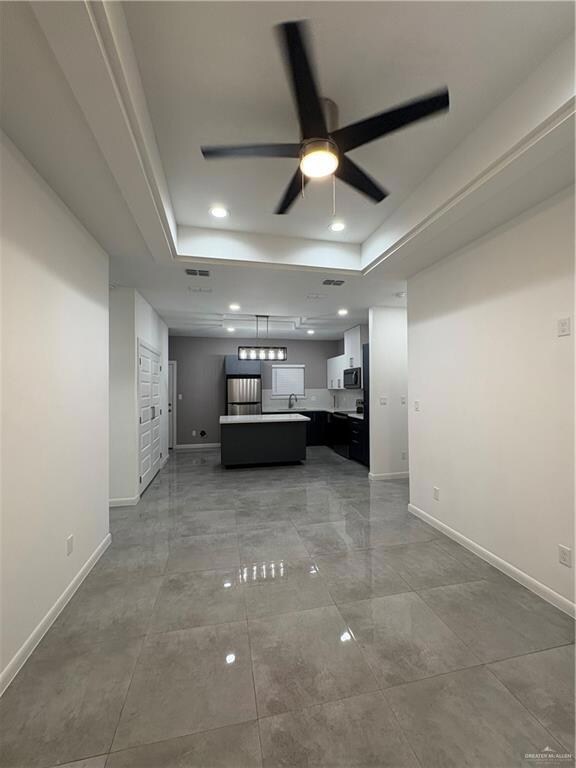 Unfurnished living room with a raised ceiling, ceiling fan, baseboards, and recessed lighting