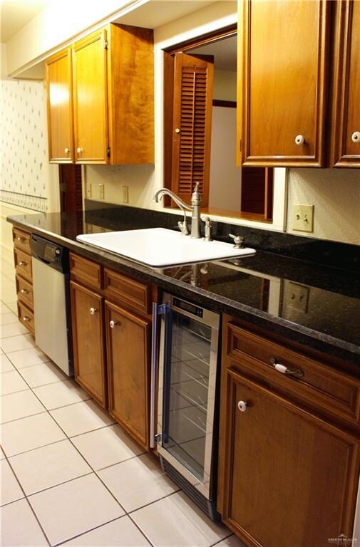 Kitchen featuring sink, dark stone countertops, wine cooler, light tile patterned flooring, and stainless steel dishwasher
