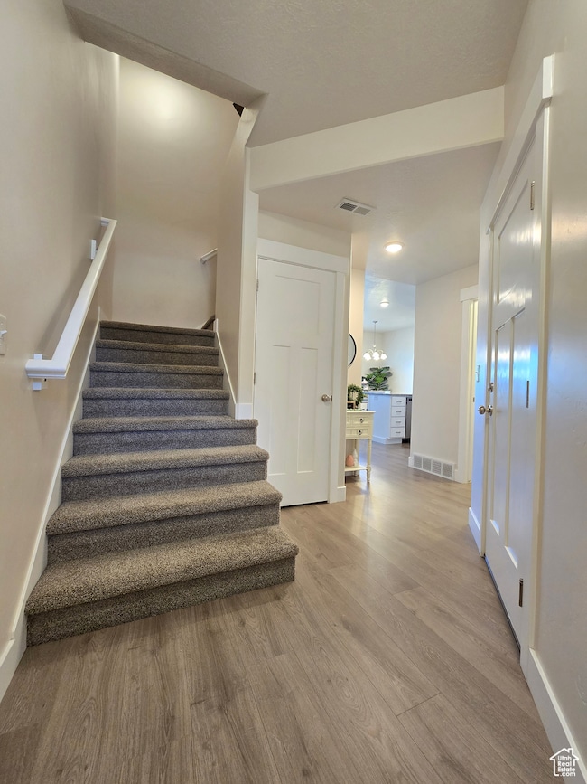 Stairs featuring wood finished floors and a chandelier