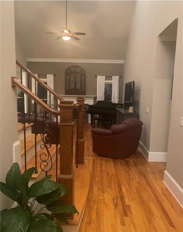 Living area with a ceiling fan, wood finished floors, stairway, and crown molding