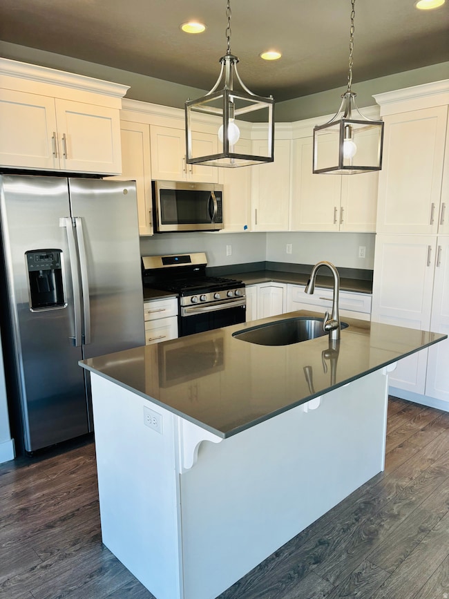Kitchen featuring appliances with stainless steel finishes, recessed lighting, an island with sink, white cabinetry, and dark wood finished floors