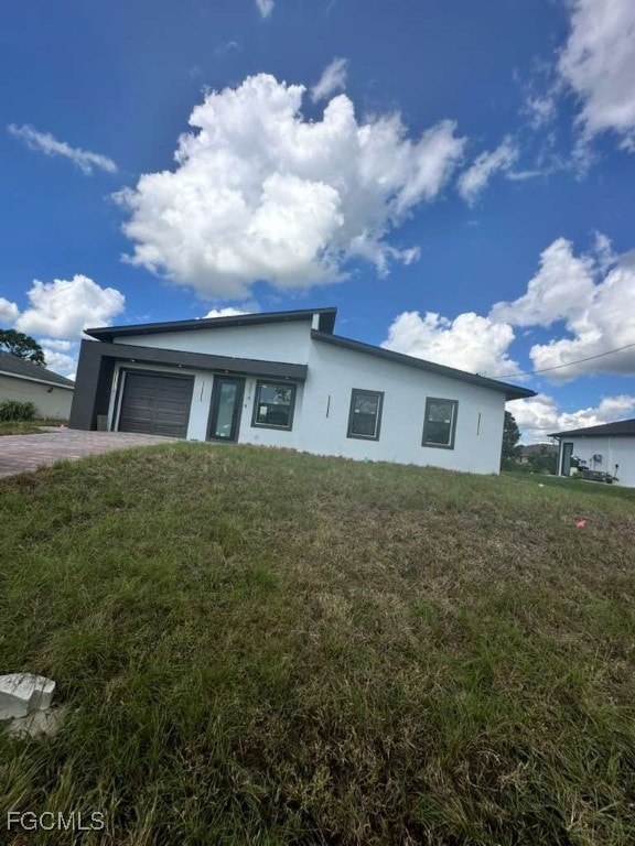 View of front of home with stucco siding, a front lawn, a garage, and driveway