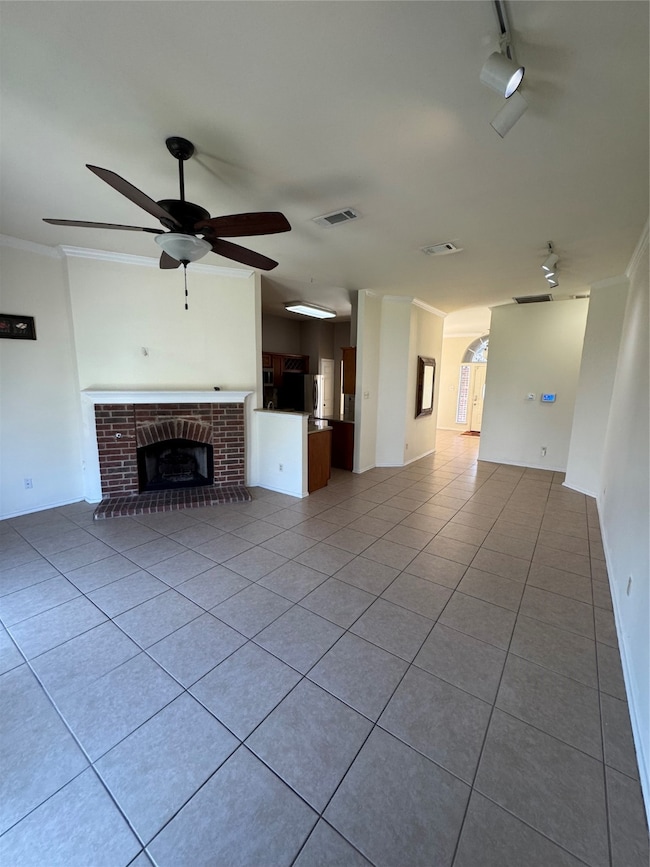 Unfurnished living room featuring light tile patterned floors, ornamental molding, a fireplace, ceiling fan, and arched walkways