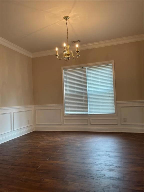Spare room with a chandelier, crown molding, wainscoting, dark wood-type flooring, and a decorative wall