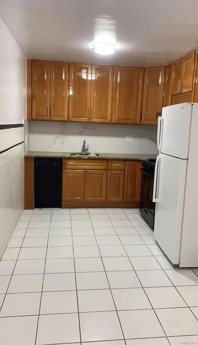 Kitchen with black appliances, brown cabinets, light tile patterned floors, and dark stone countertops