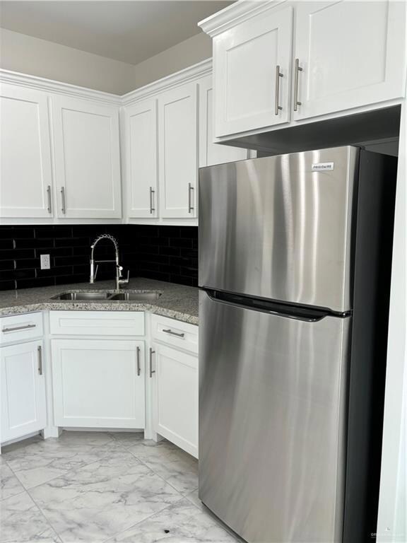 Kitchen featuring light stone countertops, refrigerator, tasteful backsplash, and white cabinetry