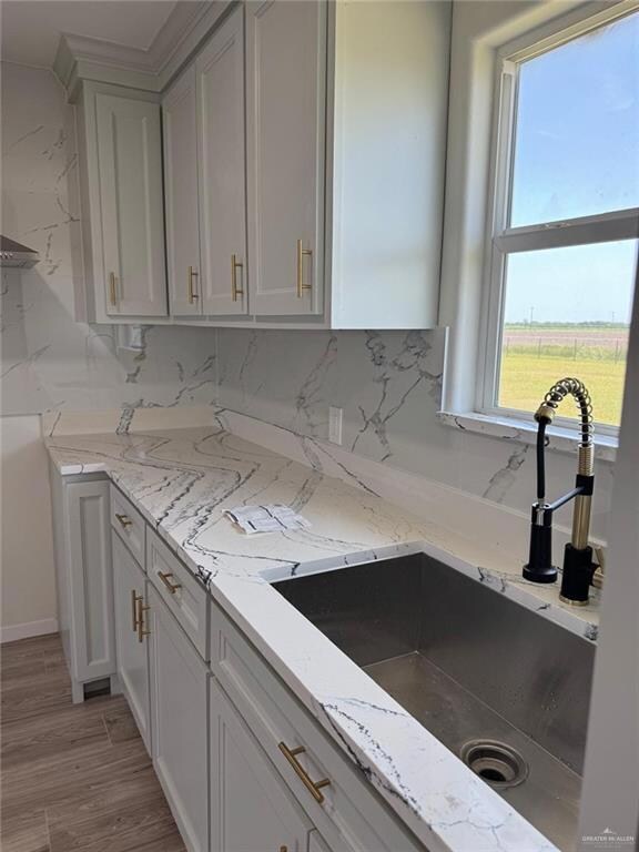 Kitchen with decorative backsplash, light stone counters, and light wood-style floors