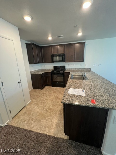Kitchen with dark brown cabinets, a peninsula, black range oven, light stone counters, and recessed lighting