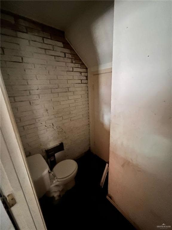 Bathroom with toilet, brick wall, and lofted ceiling