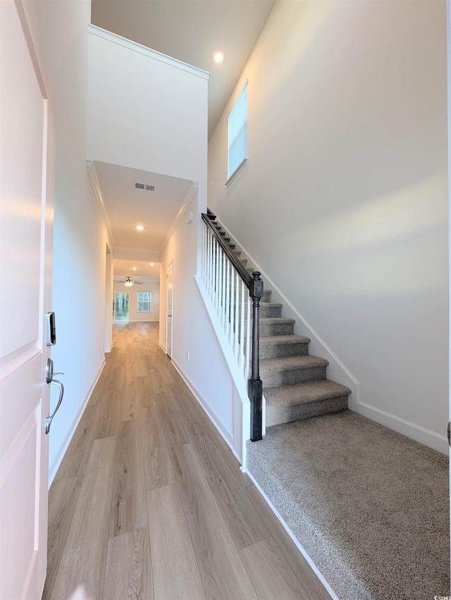 Stairway with wood finished floors, a towering ceiling, ornamental molding, and recessed lighting