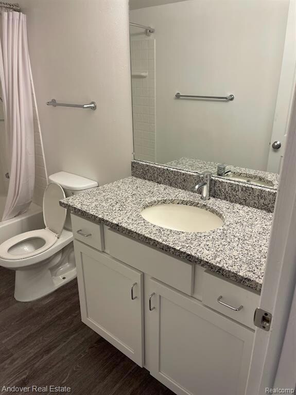 Full bath with shower / bath combo with shower curtain, vanity, and dark wood-style floors