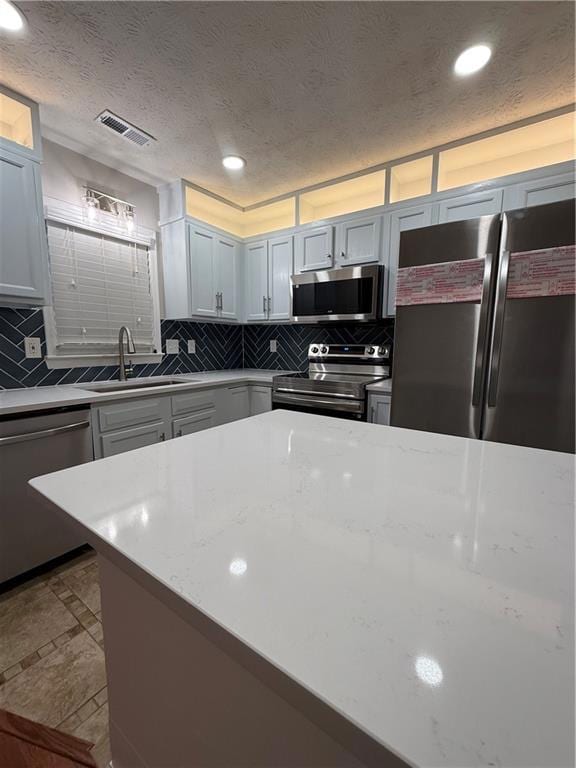 Kitchen featuring stainless steel appliances, light stone counters, recessed lighting, decorative backsplash, and a textured ceiling