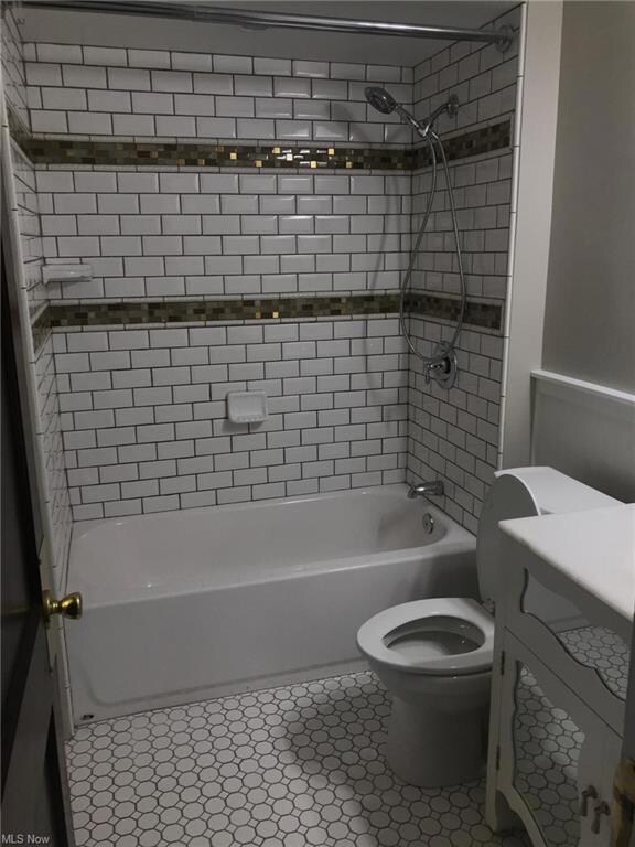 Full bathroom with light tile flooring, tiled shower / bath combo, and vanity