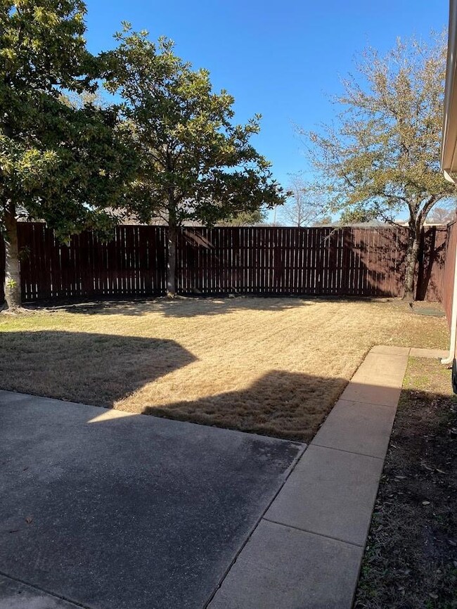 Fenced back yard with several trees. Open patio