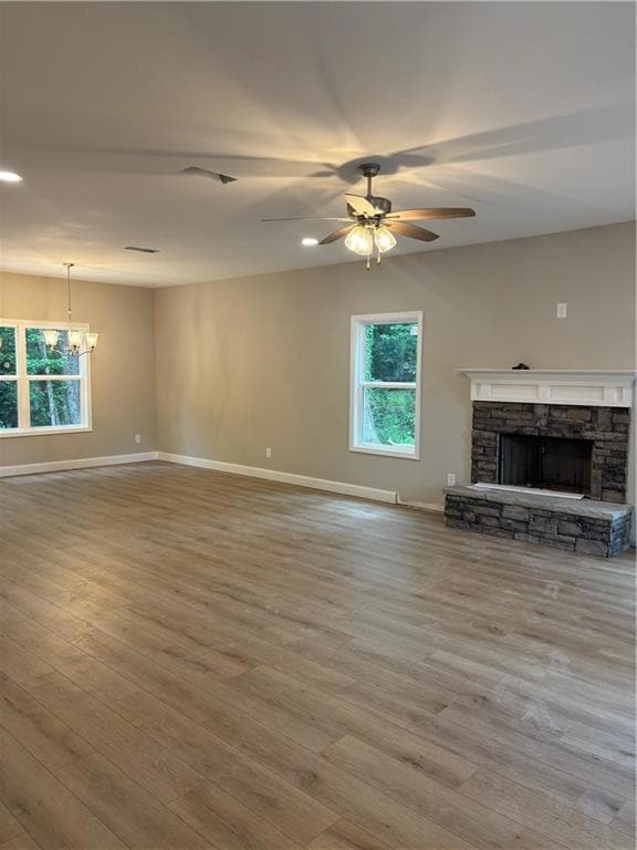 Unfurnished living room with a chandelier, a stone fireplace, ceiling fan, and wood finished floors