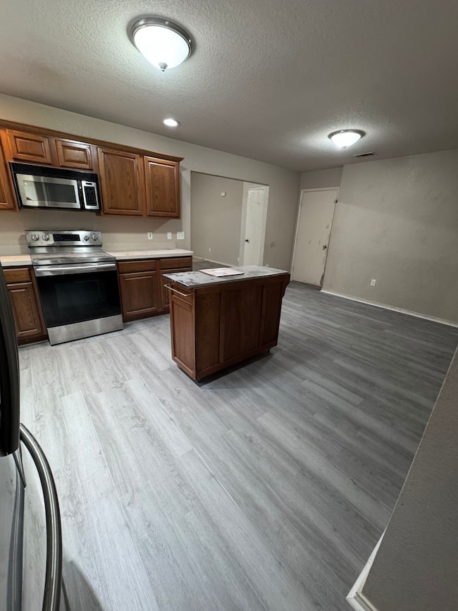 Kitchen with light wood finished floors, appliances with stainless steel finishes, a textured ceiling, light countertops, and a kitchen island