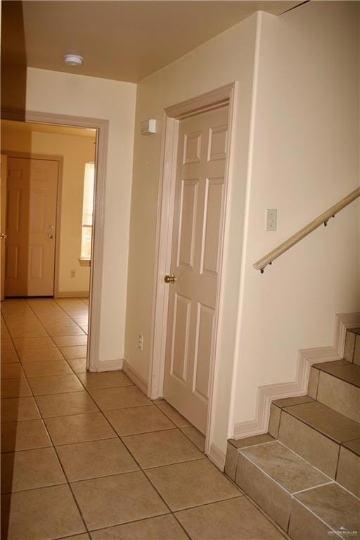 Corridor featuring light tile patterned floors, baseboards, and stairs